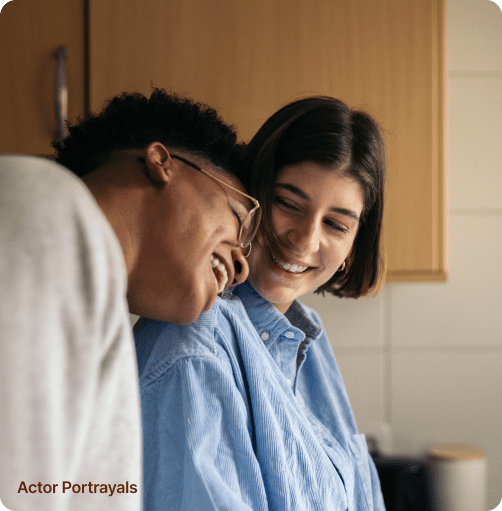 Two people sharing a joyful moment in a cozy kitchen, one with glasses laughing heartily